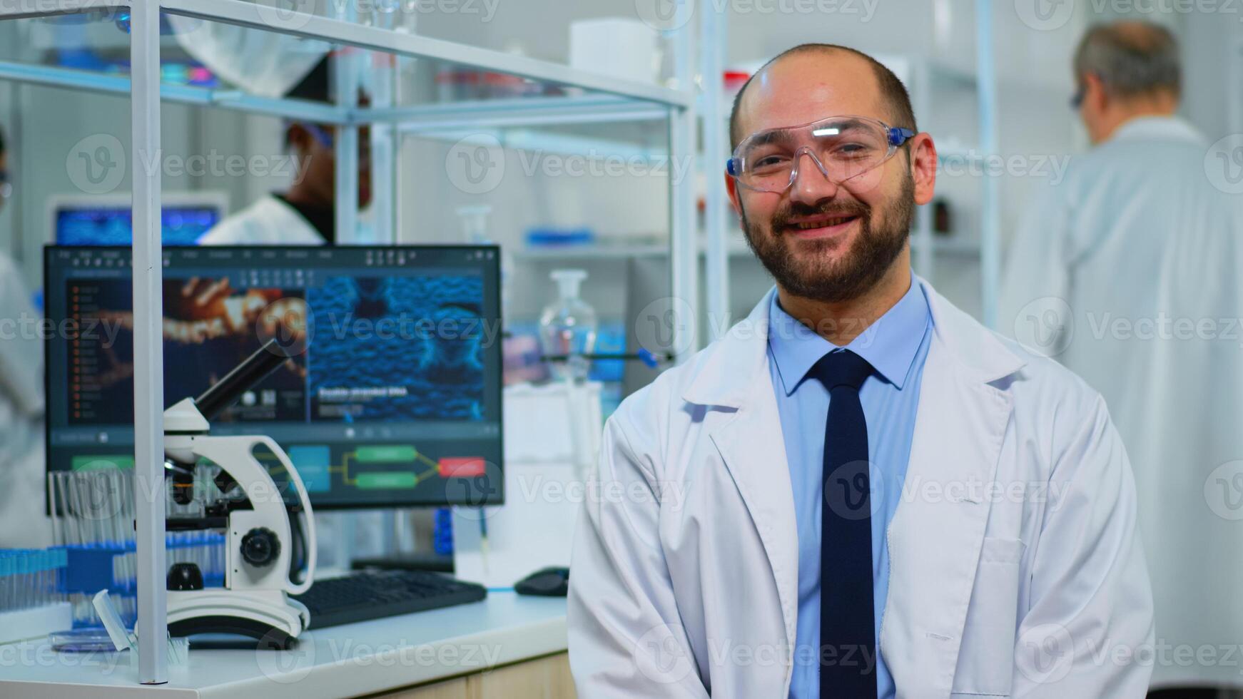 Microbiologist sitting in laboratory looking at camera in modern equipped lab. Multiethnic team examining virus evolution using high tech and chemistry tools for scientific research, vaccine development. photo