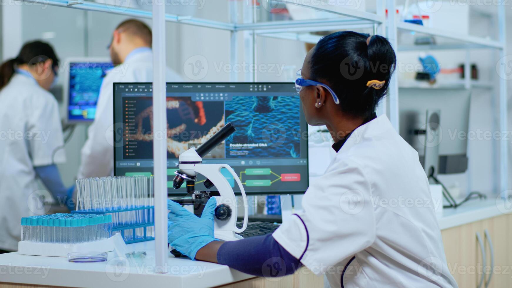 African woman scientist using microscope in modern equipped lab. Multiethnic team examining virus evolution using high tech for scientific research of treatment development against covid19. photo