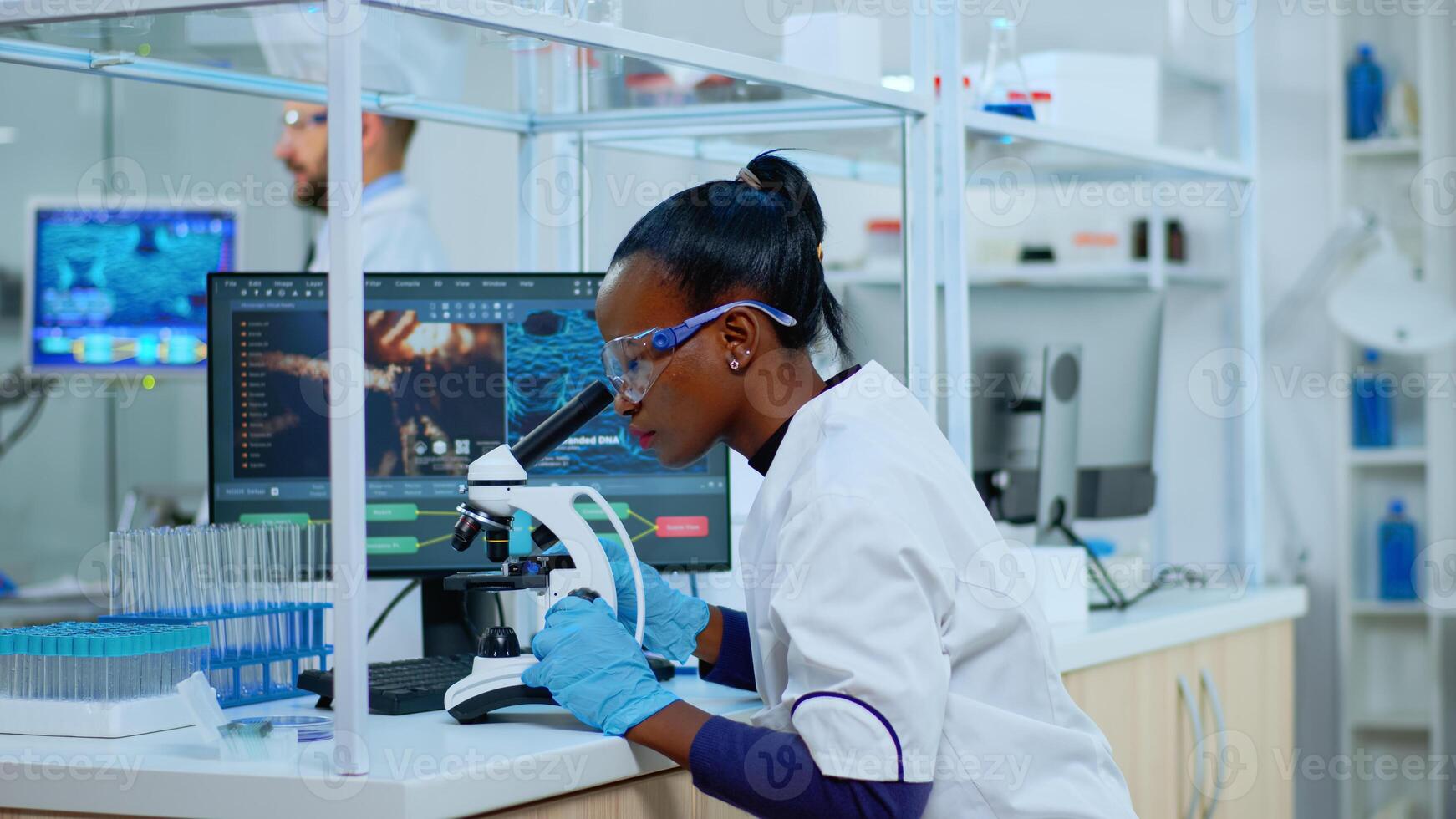 African scientist checking sample of virus using microscope in modern lab. Multiethnic team examining vaccine evolution using high tech for scientific research of treatment development against covid19 photo