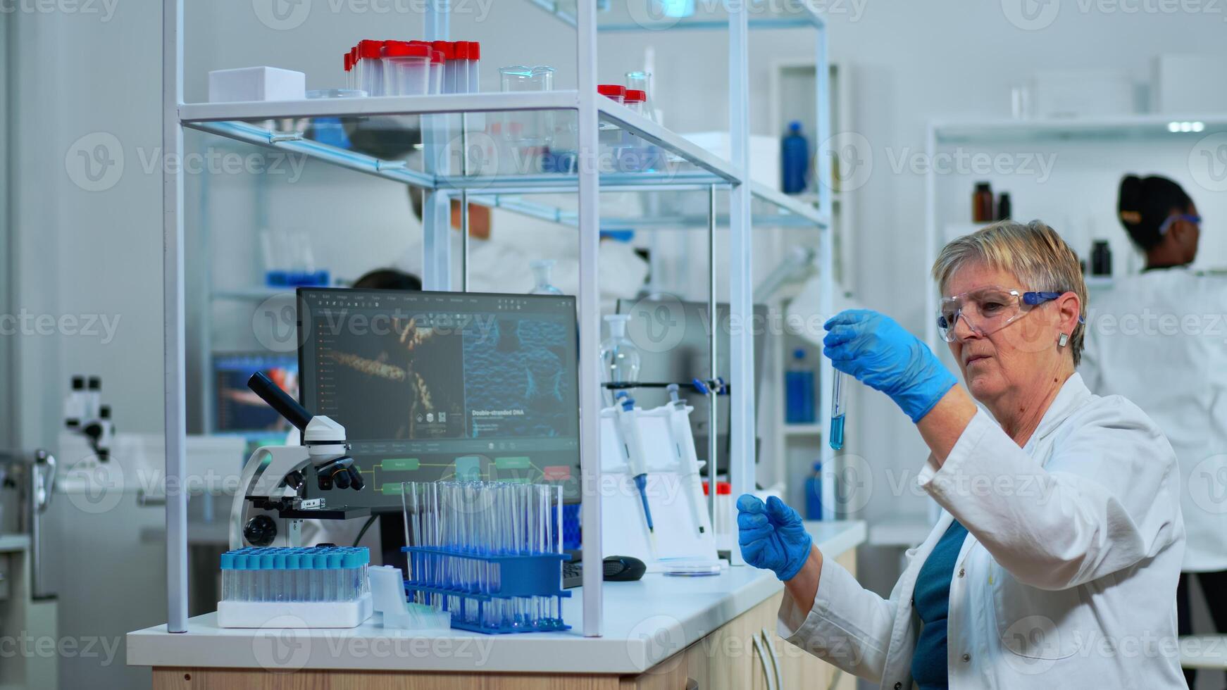 Microchemist doing research checking liquid in test tube typing results on pc in modern equipped lab. Multiethnic team examining virus evolution using high tech for vaccine development against covid19 photo