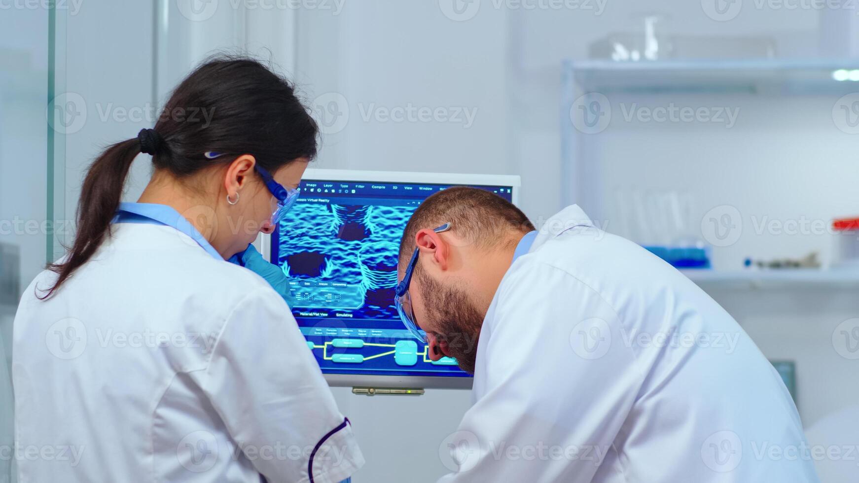 Team of scientists discussing about virus development in front of pc in modern equipped laboratory. Multiethnic stuff analysing vaccine evolution using high tech for researching treatment photo