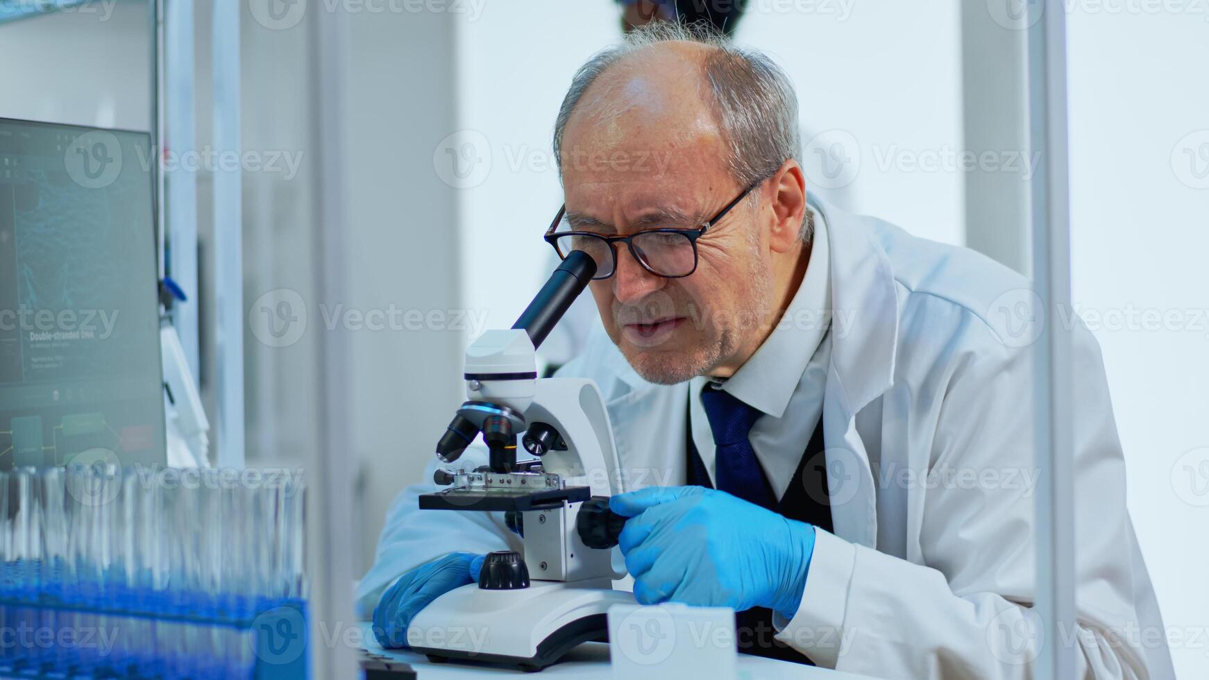 Laboratory scientist conducting experiment looking at microscope in busy modern lab. Eldery man working with various bacteria tissue, blood samples, concept of pharmaceutical research for antibiotics photo