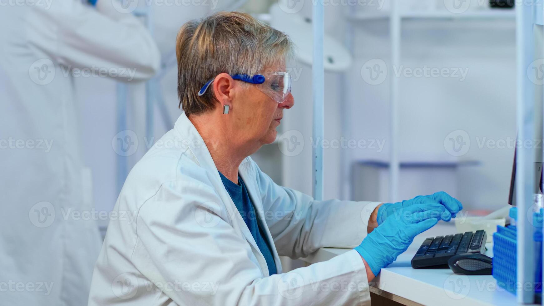 Close up of elderly chemist woman typing on computer in modern equipped laboratory. Multiethnic stuff analysing vaccine evolution using high tech for researching treatment against covid19 virus photo