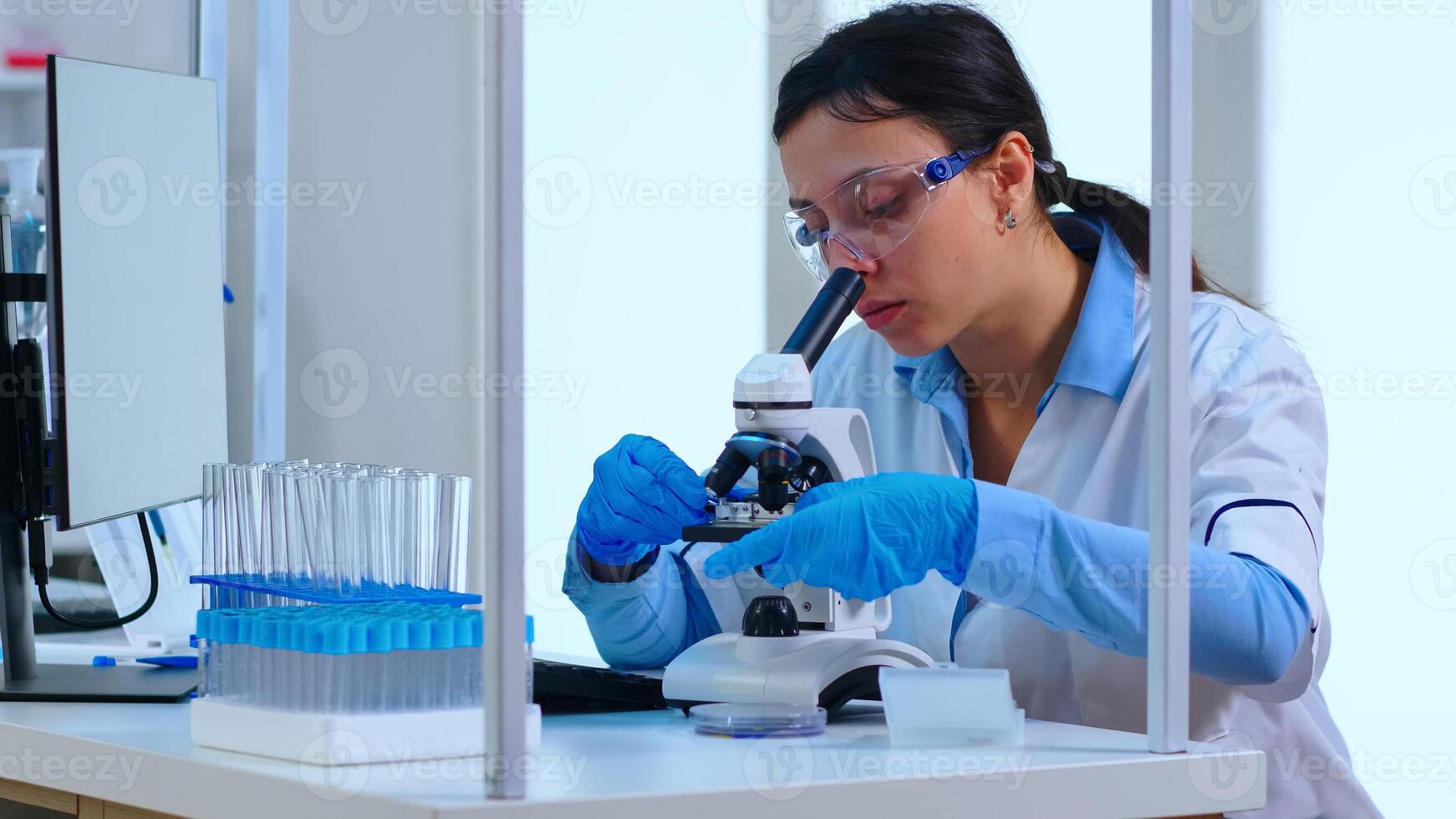 Scientist placing a slide on specimen stage of a laboratory microscope making adjustments. Chemist working with various bacteria, tissue and blood samples, pharmaceutical research for antibiotics photo