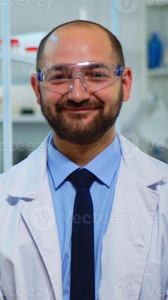 Portrait of scientist man smiling at camera sitting in modern equipped laboratory. Multiethnic team examining virus evolution using high tech and chemistry tools for scientific research, vaccine development. photo