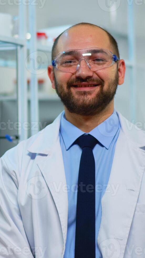 Microbiologist sitting in laboratory looking at camera in modern equipped lab. Multiethnic team examining virus evolution using high tech and chemistry tools for scientific research, vaccine development. photo