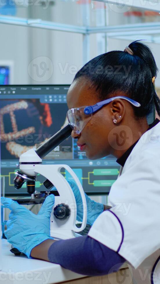 African woman scientist using microscope in modern equipped lab. Multiethnic team examining virus evolution using high tech for scientific research of treatment development against covid19. photo