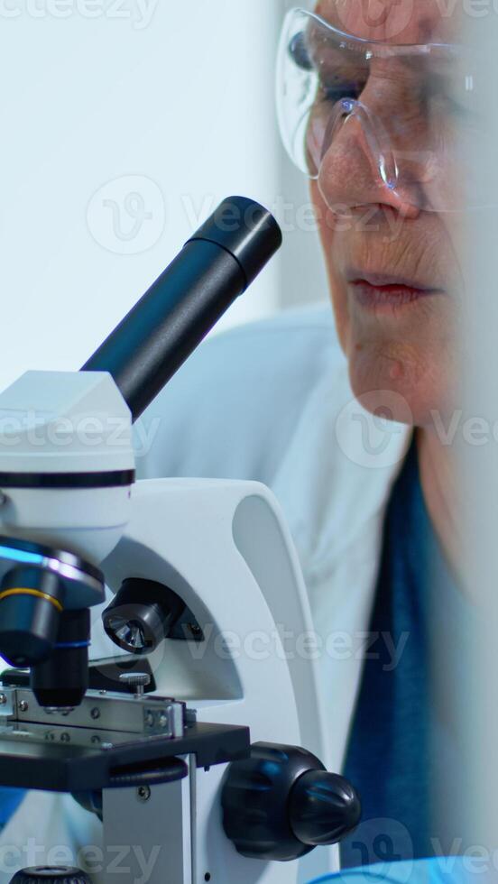 Woman research scientist looking at samples under microscope in modern equipped laboratory. Eldery doctor working with various bacteria, tissue and blood tests, pharmaceutical research for antibiotics photo