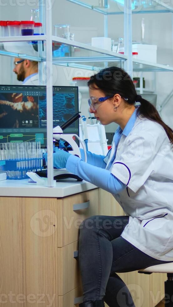 Microbiologist working for new vaccine in modern laboratory looking at samples under microscope. Multiethnic team examining virus evolution using high tech and chemistry tools for scientific research. photo