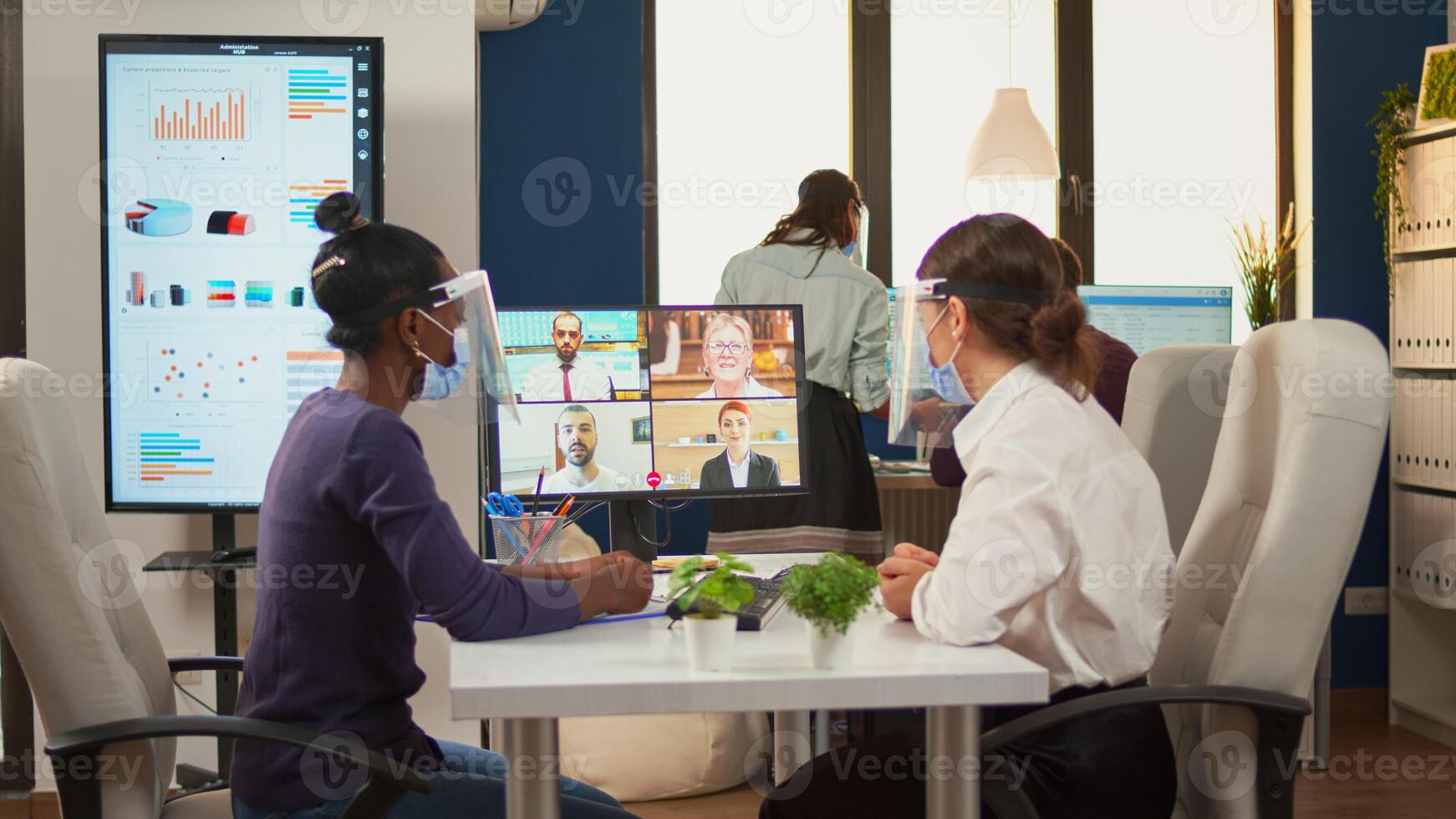 Black woman and comapany entrepreneur wearing protective masks talking with remotely colleagues on call. New normal business office Multiethnic team working respecting social distance. photo