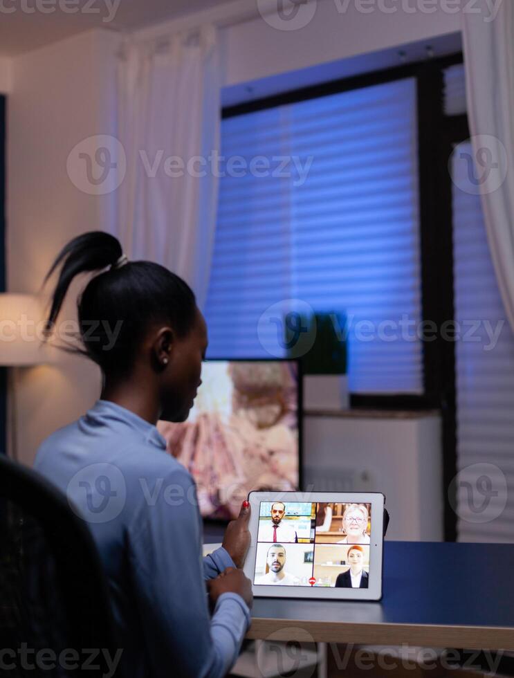 Dark skinned freelancer having werbcam conference on tablet pc from home office late at night. Lady using notebook with network wireless talking on virtual meeting . photo