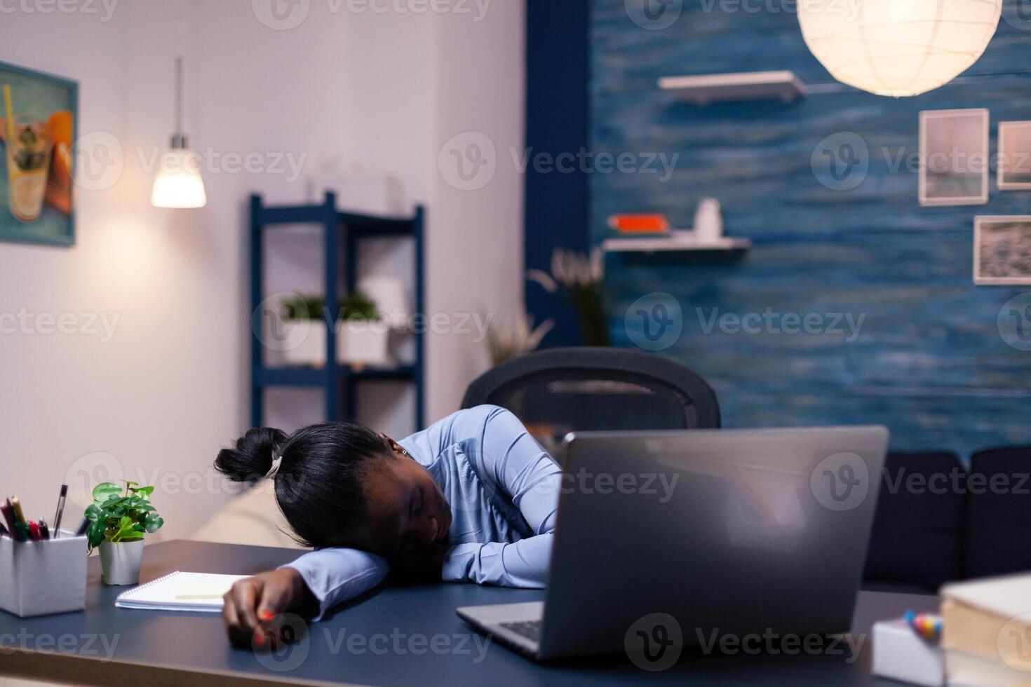 African business woman sleeps during late night hourse in the course of deadline working from home. Busy employee using modern technology network wireless doing overtime sleeping on table. photo
