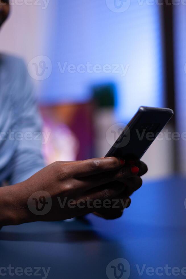 Close up of african businesswoman writing list of tasks for business project in notebook sitting at desk. Employee using modern technology network wireless doing overtime. photo