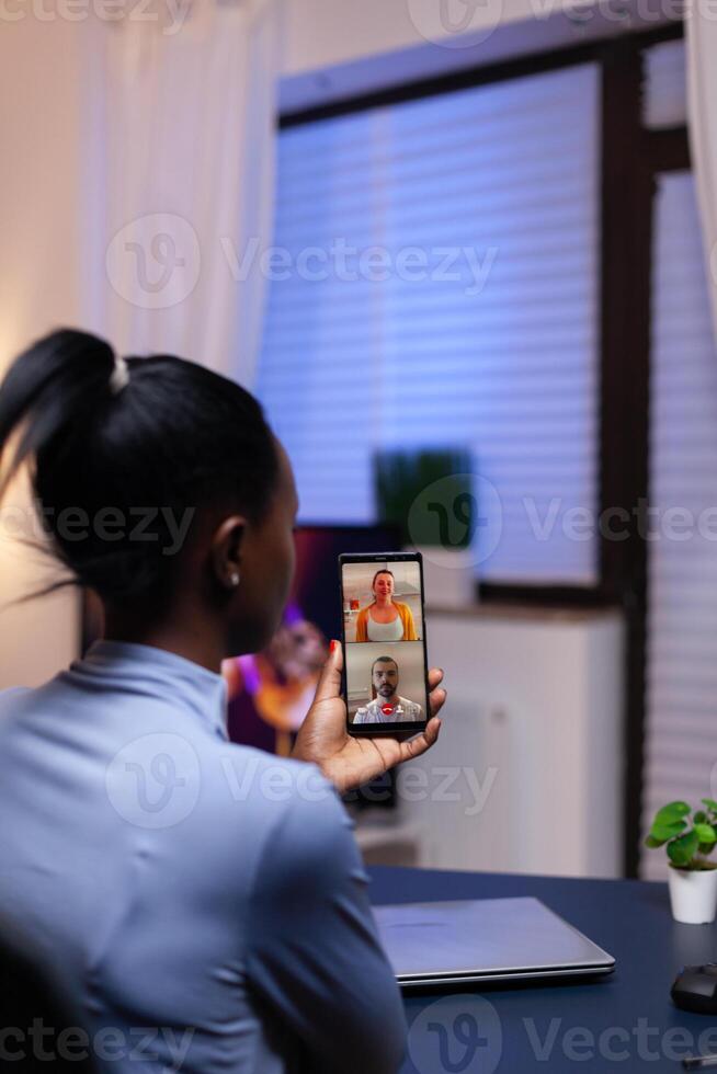 Happy coworkers talking and consulting each other in the course of conference on smartphone. Busy employee using modern technology network wireless doing overtime for job. photo