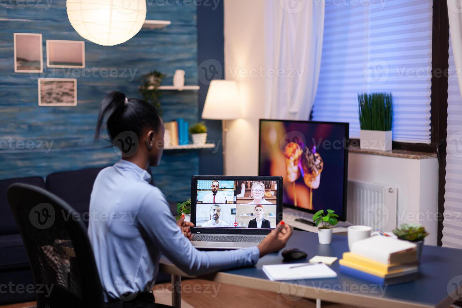 Dark skinned entrepreneur consulting with colleagues remotely from home late in the evening. Using modern technology network wireless talking on virtual meeting doing overtime. photo
