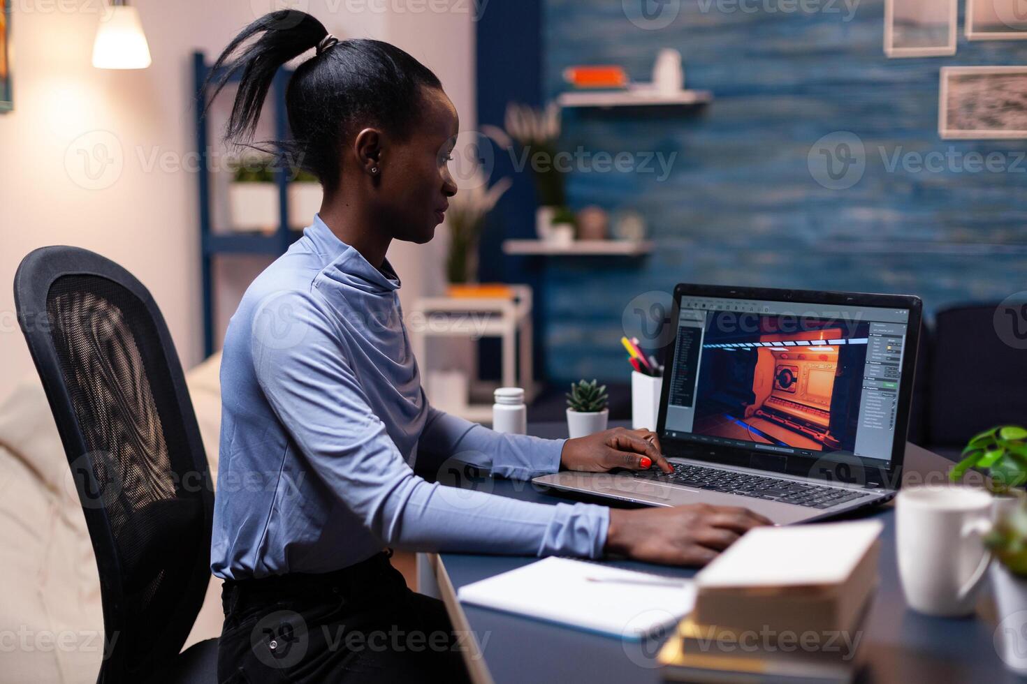 Dark skinned gamer testing game using laptop at night in home office. Professional player checking digital games on her computer with modern technology network wireless. photo