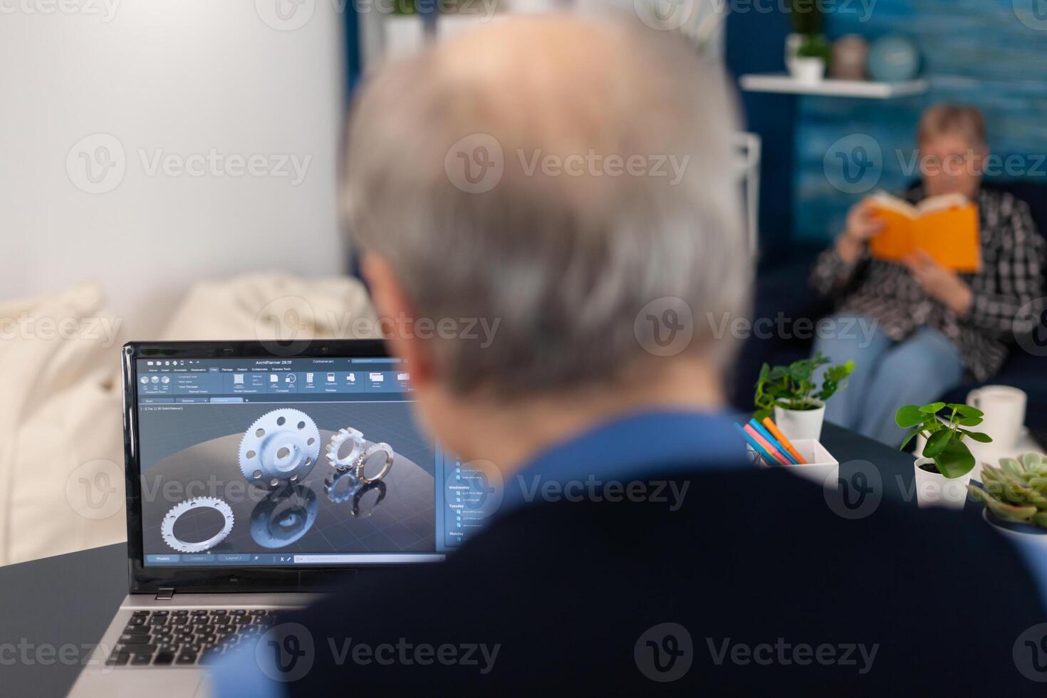 Engineer designed gears parts using professional software. Experienced engineer working from home office on mechanical project using laptop computer technology and wife is reading a book on sofa. photo