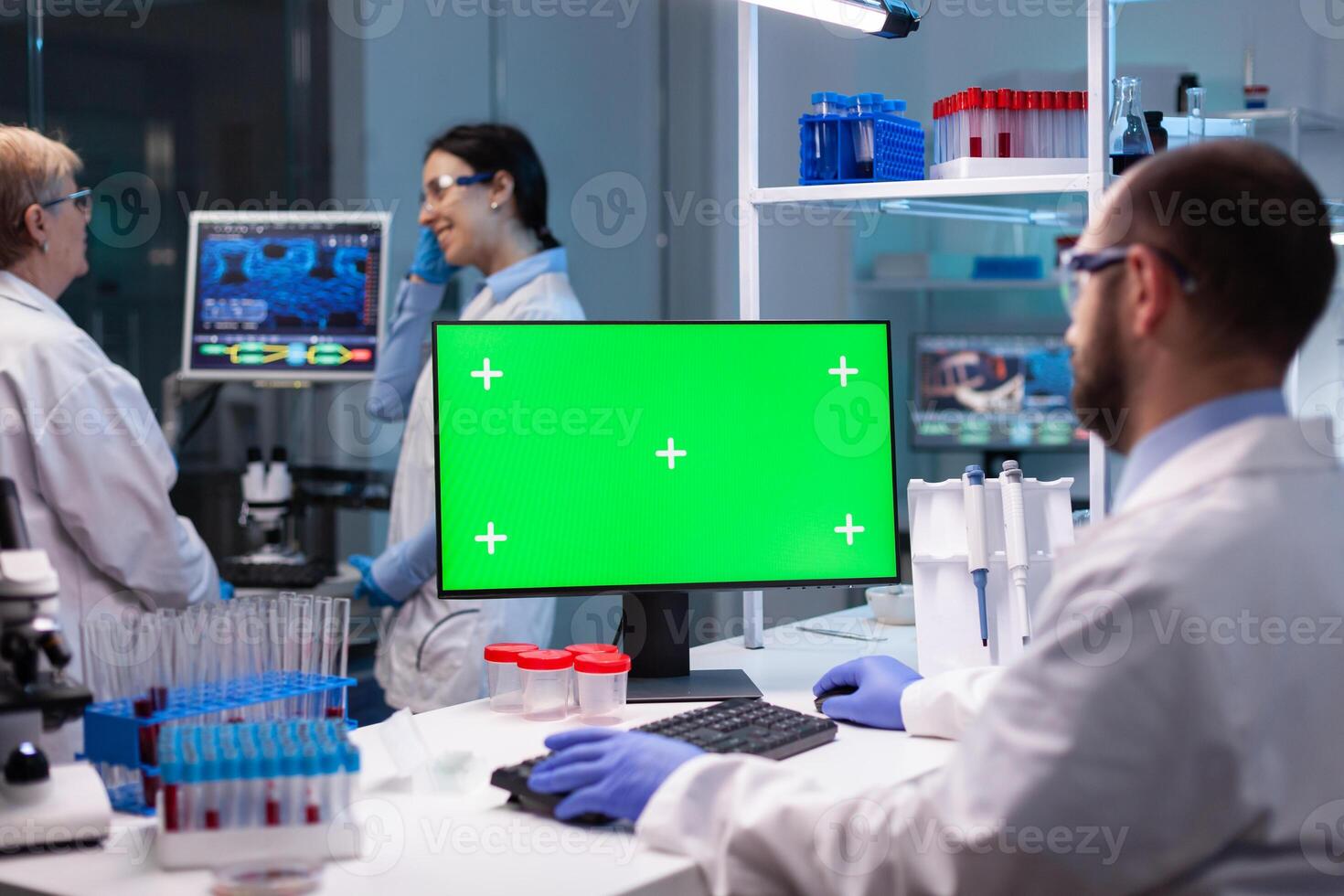 Biochemist working in laboratory using green mock-up screen for biochemistry experiment with chroma key monitor. Team of microbiologists doing vaccine analysis and discovery treatment cure against covid19 photo