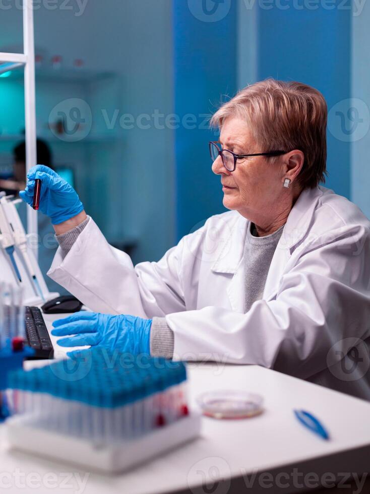 Senior chemist scientist doing experiment with blood in test tube. Researcher in medicine lab working with professional technology equipment for diagnostics development and healthcare. photo