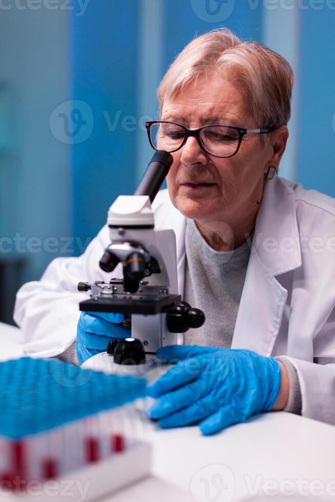 Senior scientist looking through microscope at sample in biology lab. Laboratory for scientific research with professional equipment for virus study and diagnosis biotechnolog development. photo