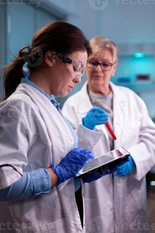 Team of scientist discussing blood analyzis using tablet pc, development. Specialist team of medical researchers working in sterile lab wearing protection glasses. photo