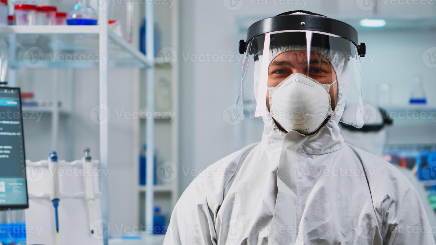 Portrait of scientist man wearing coverall smiling at camera sitting in modern equipped laboratory. Chemist doctor xamining virus evolution using high tech for scientific research, vaccine development photo