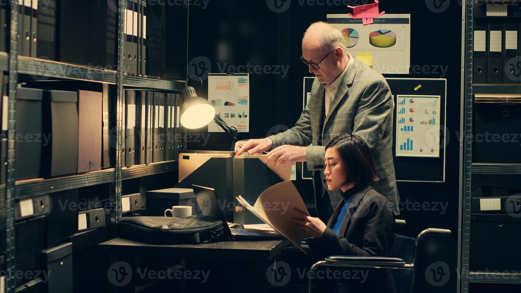 Wheelchair user and inspector analyzing criminal records in police archive room, cross reference data from cases to identify similarities. Team of agents compile notes on crime trends. Camera A. photo