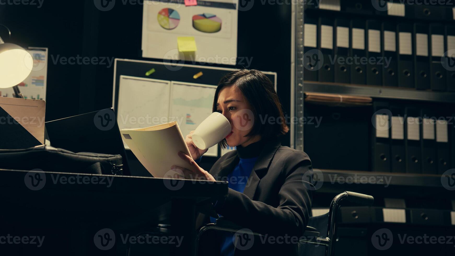 Private agent studying criminal files and archived folders in incident room, working on legal investigation to build suspects profile. Wheelchair user reading statements and reports. Camera B. photo
