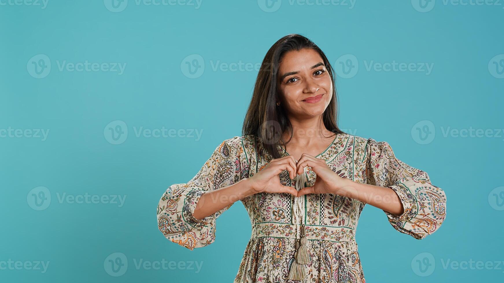 Portrait of jolly friendly indian woman doing heart symbol shape gesture with hands. Cheerful nurturing person showing love gesturing, isolated over studio background, camera A photo