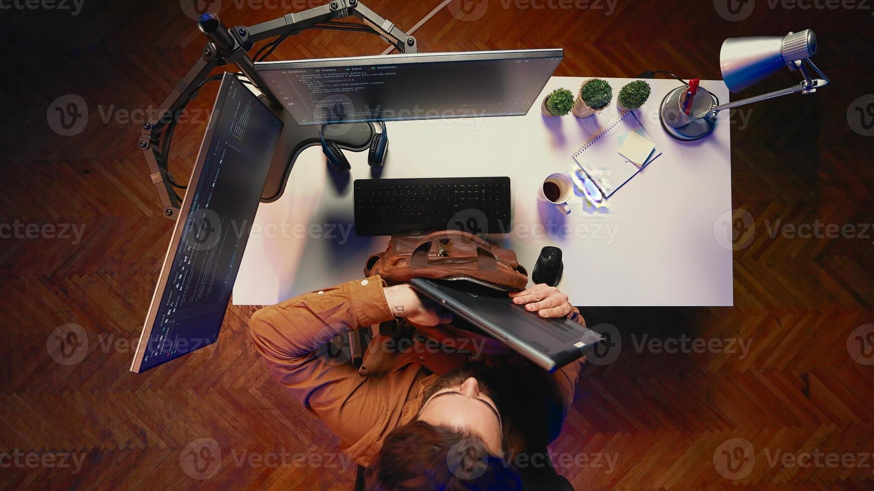 Top down view of software programmer finishing remote job shift, packing backpack, leaving office after finishing project. Aerial shot of IT admin putting laptop in bag, sitting up from desk chair photo