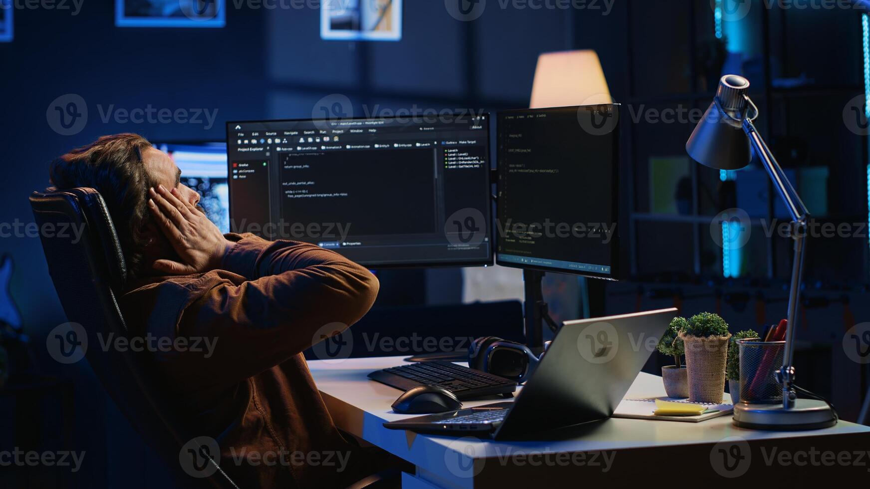 Fatigued software programmer working overnight at home, taking break from coding to stretch at desk chair. Overworked IT professional feeling exhausted, pausing tasks to rest, camera A photo