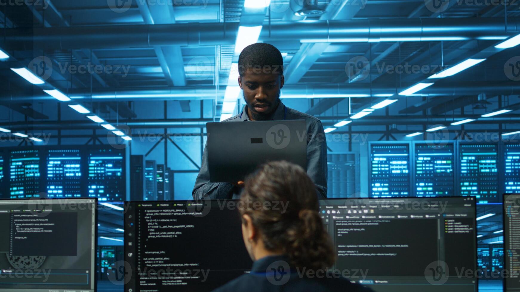 Smiling african american manager in data center doing checkup on electronics to avoid downtime. Team leader holding laptop supervising employees in server room infrastructure components photo