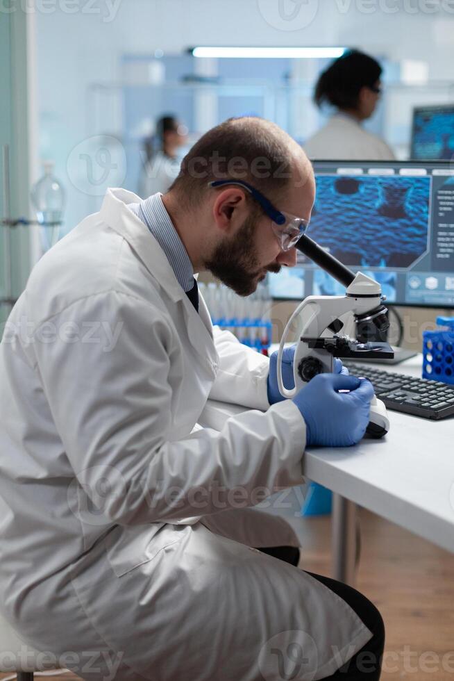 Biologist scientist man doctor examining coronavirus sample results using medical microscope developing virus vaccine. Biochemistry investigation in scientific hospital laboratory. Biomedical industry photo