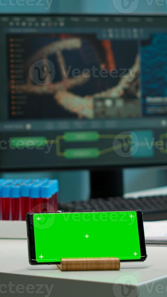 Horizontal mobile phone with green screen working in labooratory with mock up template, chroma key display while professional engineer testing virus evolution in background. High tech development lab. photo