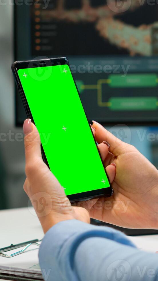 Medic in scientific laboratory holding phone with greenscreen wearing white coat while nurse bringing blood samples. Healthcare specialist in modern lab using smartphone with mockup chroma key display photo