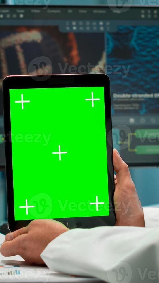 Male chemist scientist holding green mock-up screen tablet sitting at desk. In background technology research, development laboratory with specialist doctor working in high tech design photo