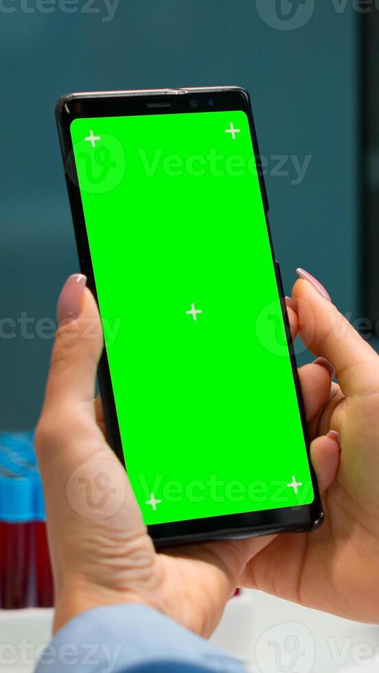 Close up of doctor's hand holding phone with green screen sitting at desk in biological laboratory while nurse bringing blood samples. Scientist using smartphone with mockup, chroma key display photo
