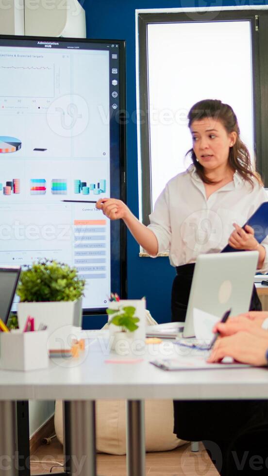 Female executive leader coach presenter giving financial presentation in modern office boardroom for corporate employees group, speaker mentor explaining training professional team at business seminar photo