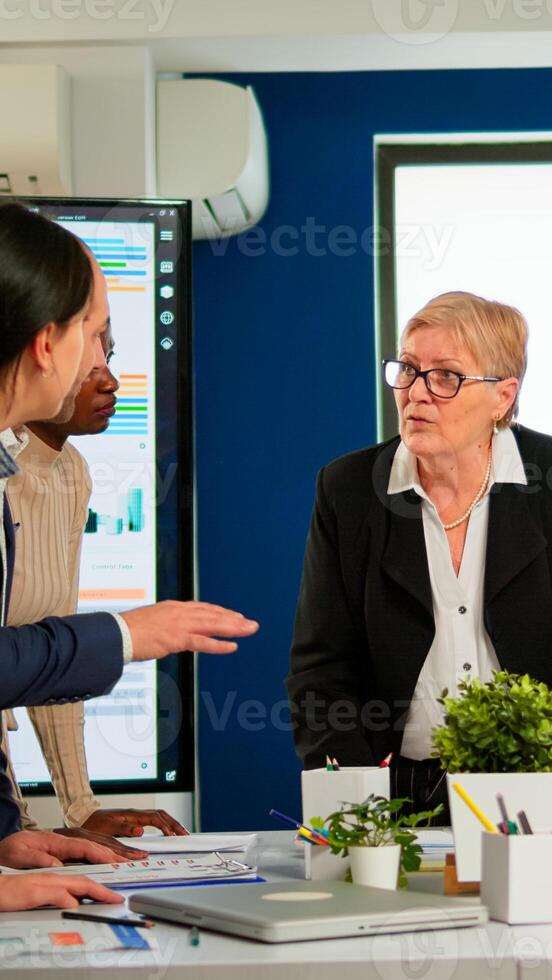 Group of diverse enthusiastic business people, marketing professionals, discussing project ideas during conference meeting, brainstorming startup company strategy sitting at office desk in broadroom photo