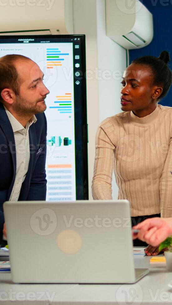 International business team talking to african woman mentor discussing company development plan standing at broadroom. Black leader explainig project strategy to diverse multiracial corporate group photo