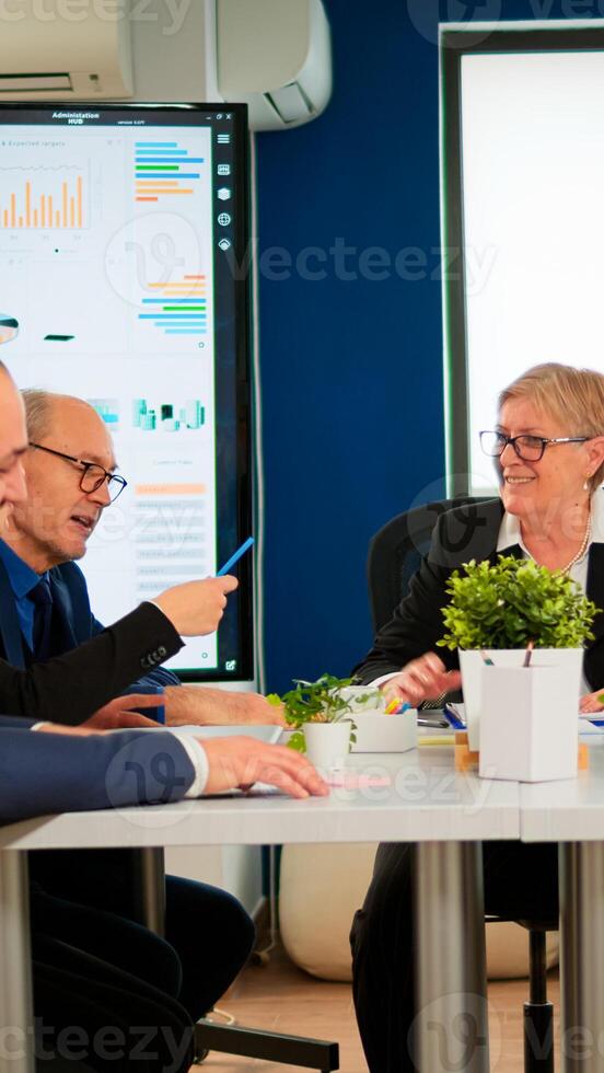 Senior woman manager waiting team for business conference meeting sitting in broadroom at table. Executive director briefing multiethnical people, explaining start up financial reports photo