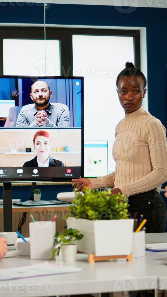 Black manager woman talking with remotely colleagues on call at tv screen, presenting new business partners. Confident businesswoman talking to web cam streaming webcast training, doing online conference call photo