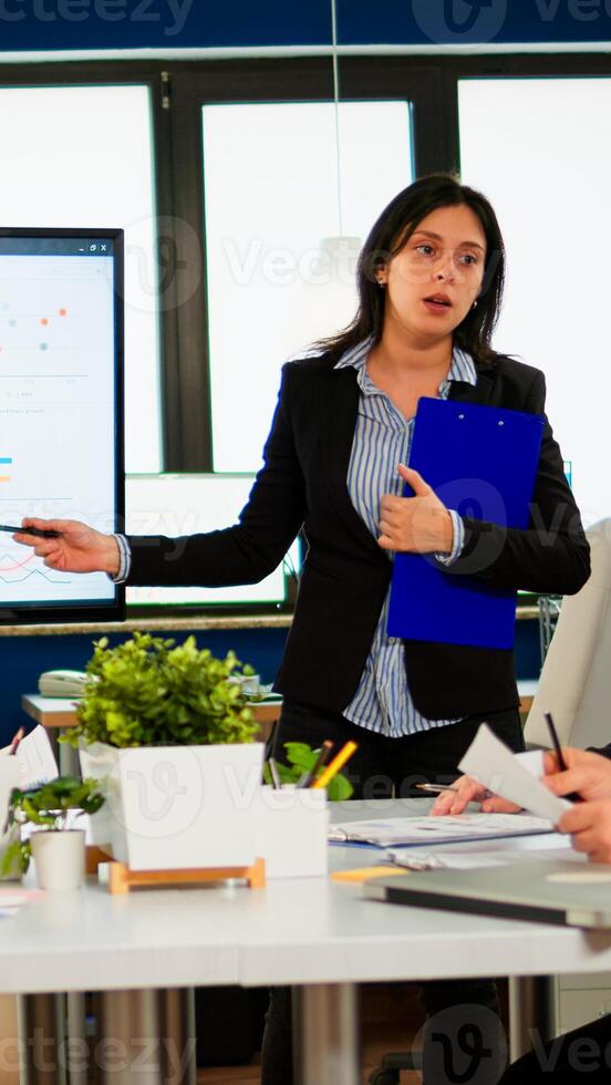 Female project manager holding financial meeting showing statistical graphs and charts on interactive whiteboard touchscreen device. Executive director working in broadroom of creative agency. photo