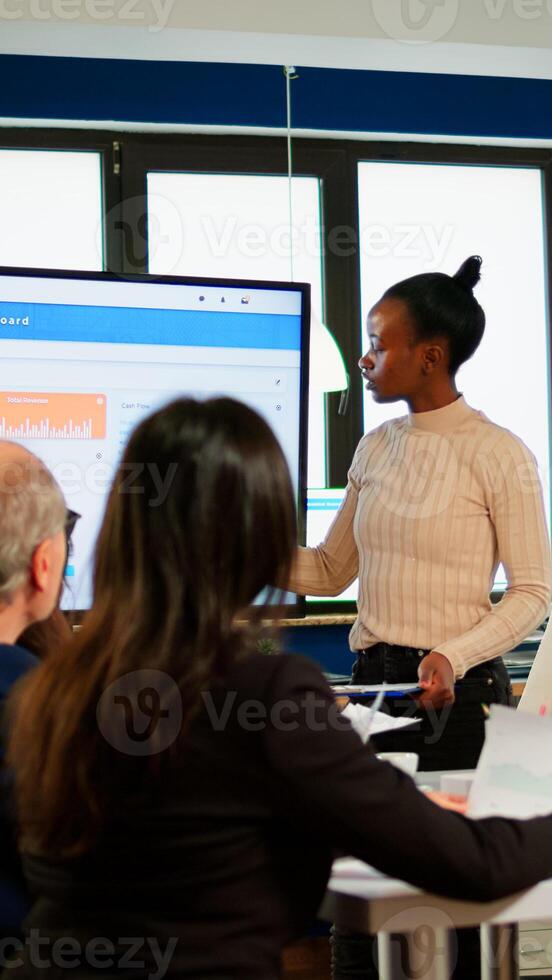 African project manager holding financial meeting showing statistical graphs and charts on interactive whiteboard touchscreen device. Executive director working in broadroom of creative agency. photo
