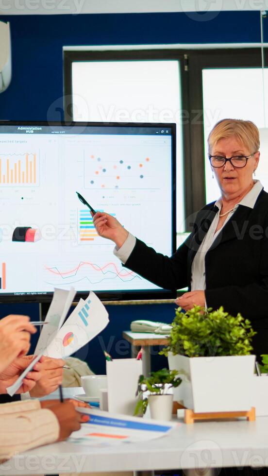 Chief analyst holding meeting presentation for a team of economists. Manager showing digital interactive whiteboard with growth analysis, charts, statistics, data, diverse people working in broadroom photo