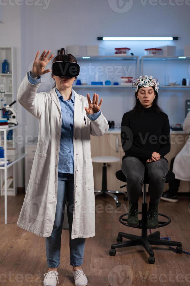 Neurologist doctor with virtual reality headset analyzing brain activity during neuroscience experiment in medical laboratory. Woman patient with eeg scanner having neurology disease photo