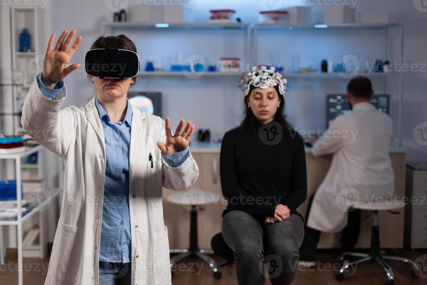 Neurologist specialist doctor with virtual reality headset analyzing brain evolution during neuroscience experiment in medical laboratory. Woman patient with eeg scanner having neurology disease photo