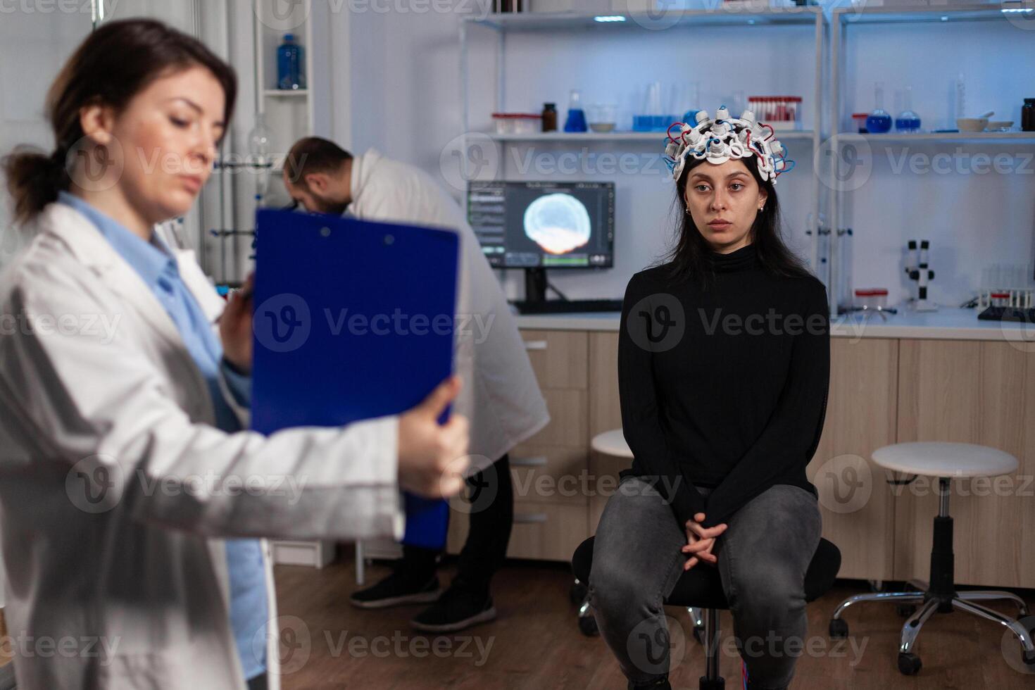 Specialist neurologist holding clipboard with tomography information on it during neuroscience experiment in modern laboratory. Researcher doctor monitoring brain activity of patient with eeg headset photo