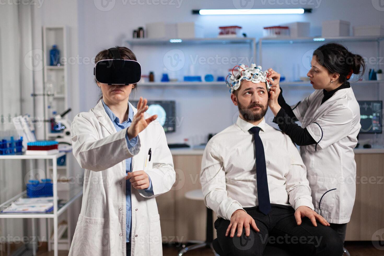 Physician doctor with virtual reality headset while neurologist woman adjusting eeg scanner of man patient analyzing brain evolution during neurology experiment. Scientist engineer using high tech photo
