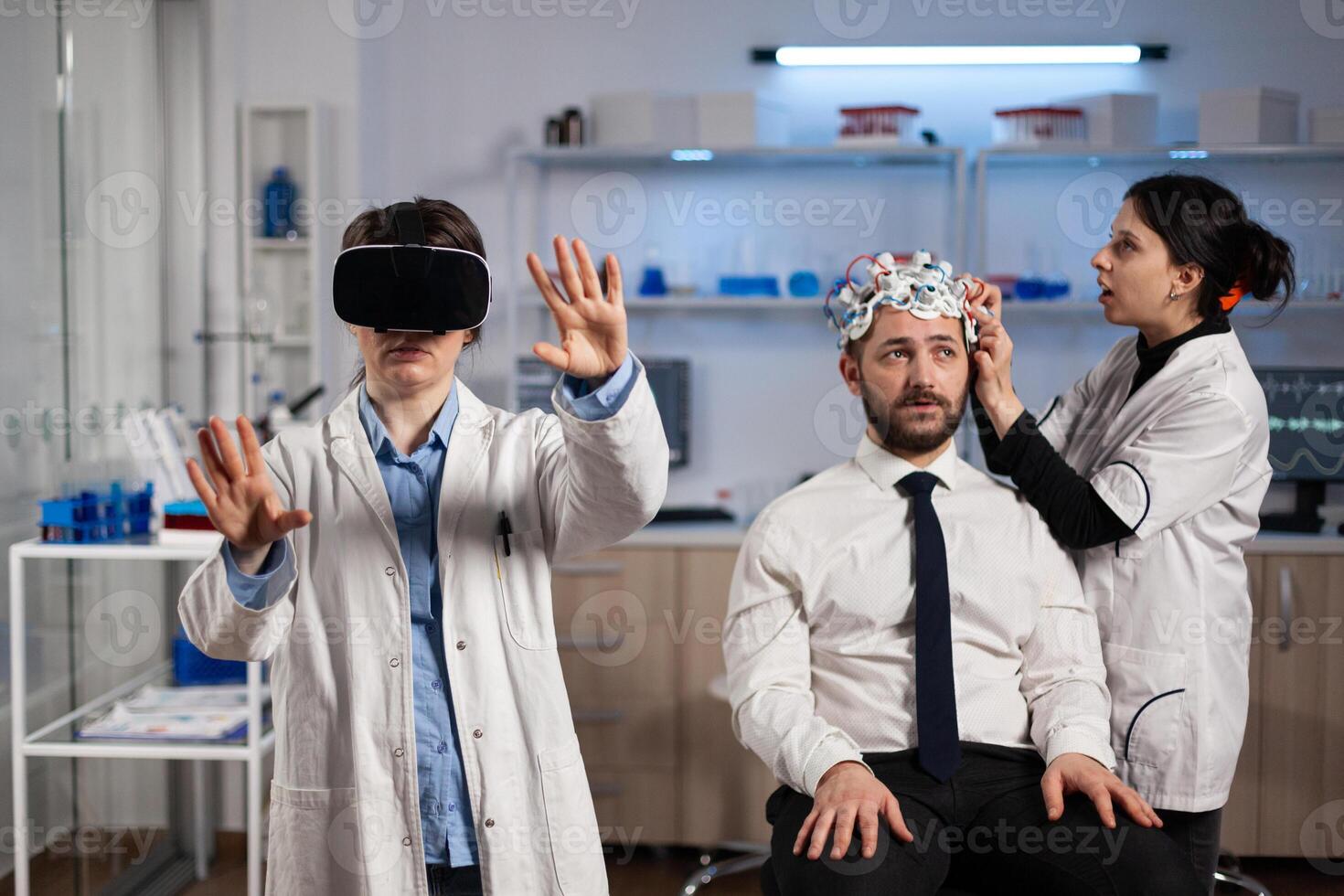Neurologist doctor wearing virtual reality headset while researcher woman adjusting eeg scanner of man patient analyzing brain activity during neurology experiment. Scientist engineer using high tech photo